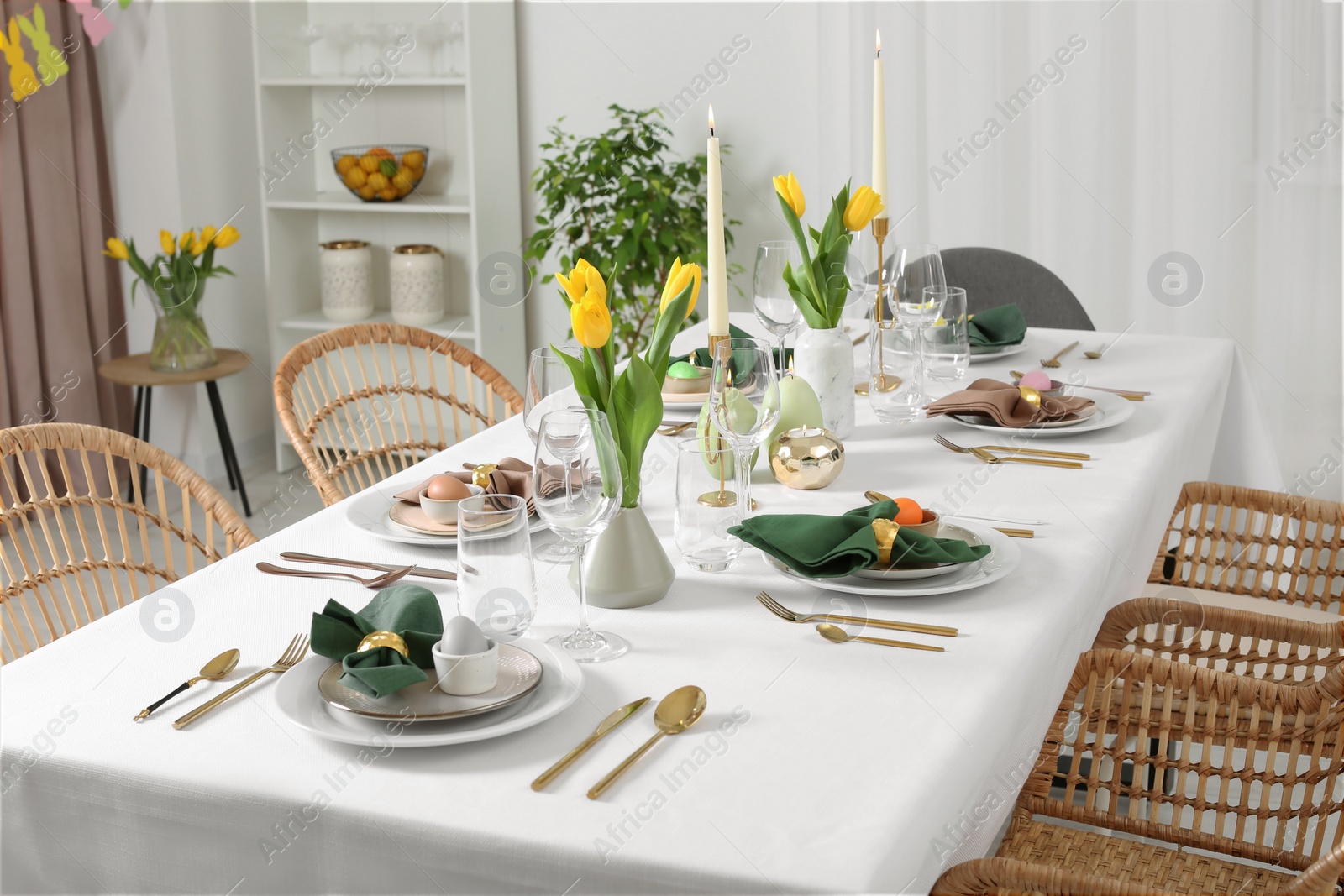 Photo of Festive Easter table setting with painted eggs, burning candles and yellow tulips in room