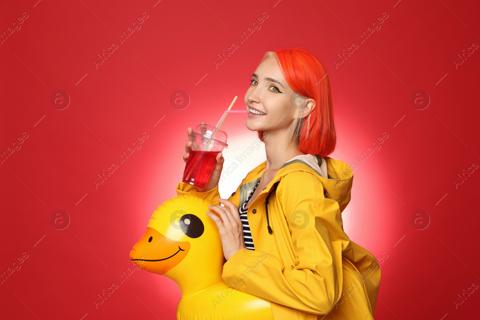 Photo of Beautiful young woman with bright dyed hair and inflatable ring drinking refreshing cocktail on color background