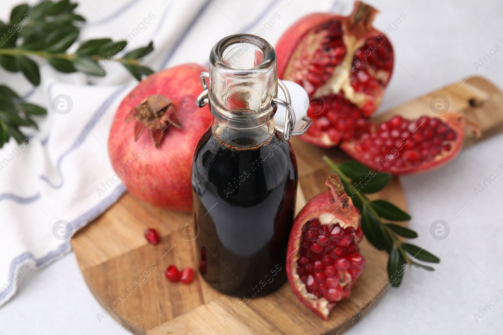 Photo of Tasty pomegranate sauce in bottle, branches and fruits on light table, closeup