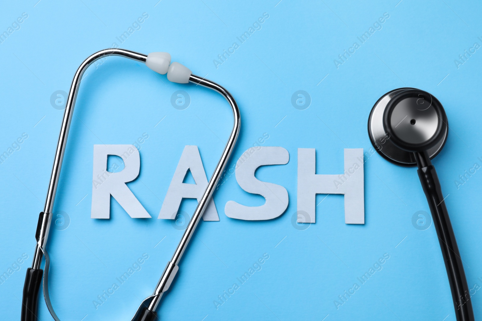 Photo of Word Rash made of paper letters and stethoscope on light blue background, flat lay