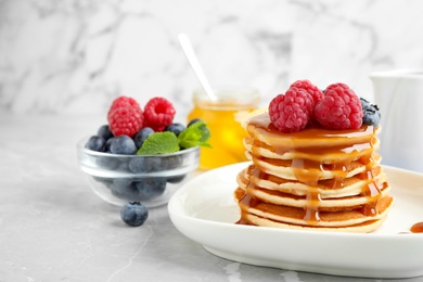 Delicious pancakes with fresh berries and syrup on grey table