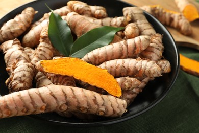 Photo of Bowl with raw turmeric roots and green leaves on table, closeup