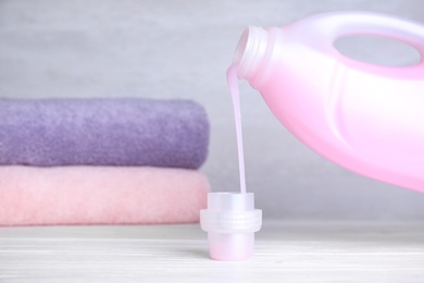 Pouring laundry detergent from bottle into cap on table, space for text