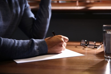 Man writing letter at wooden table indoors, closeup