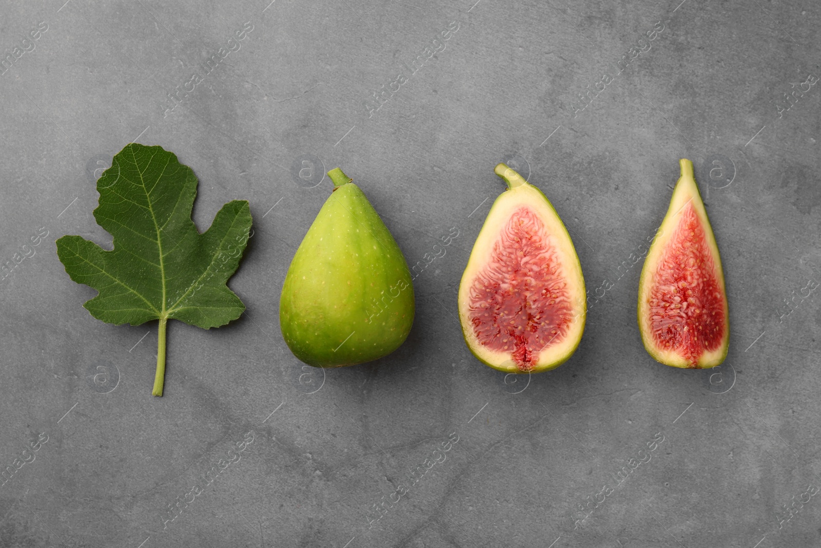 Photo of Cut and whole green figs with leaf on light gray table, flat lay