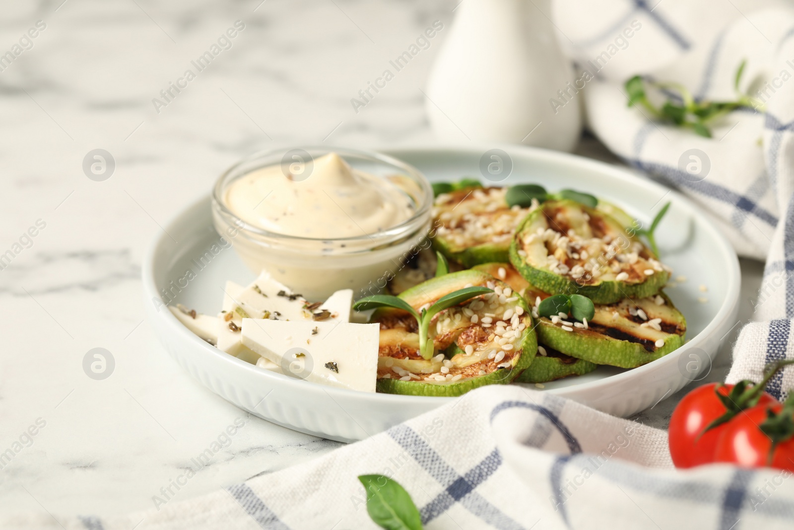 Photo of Delicious grilled zucchini slices served with sauce and cheese on white marble table, closeup