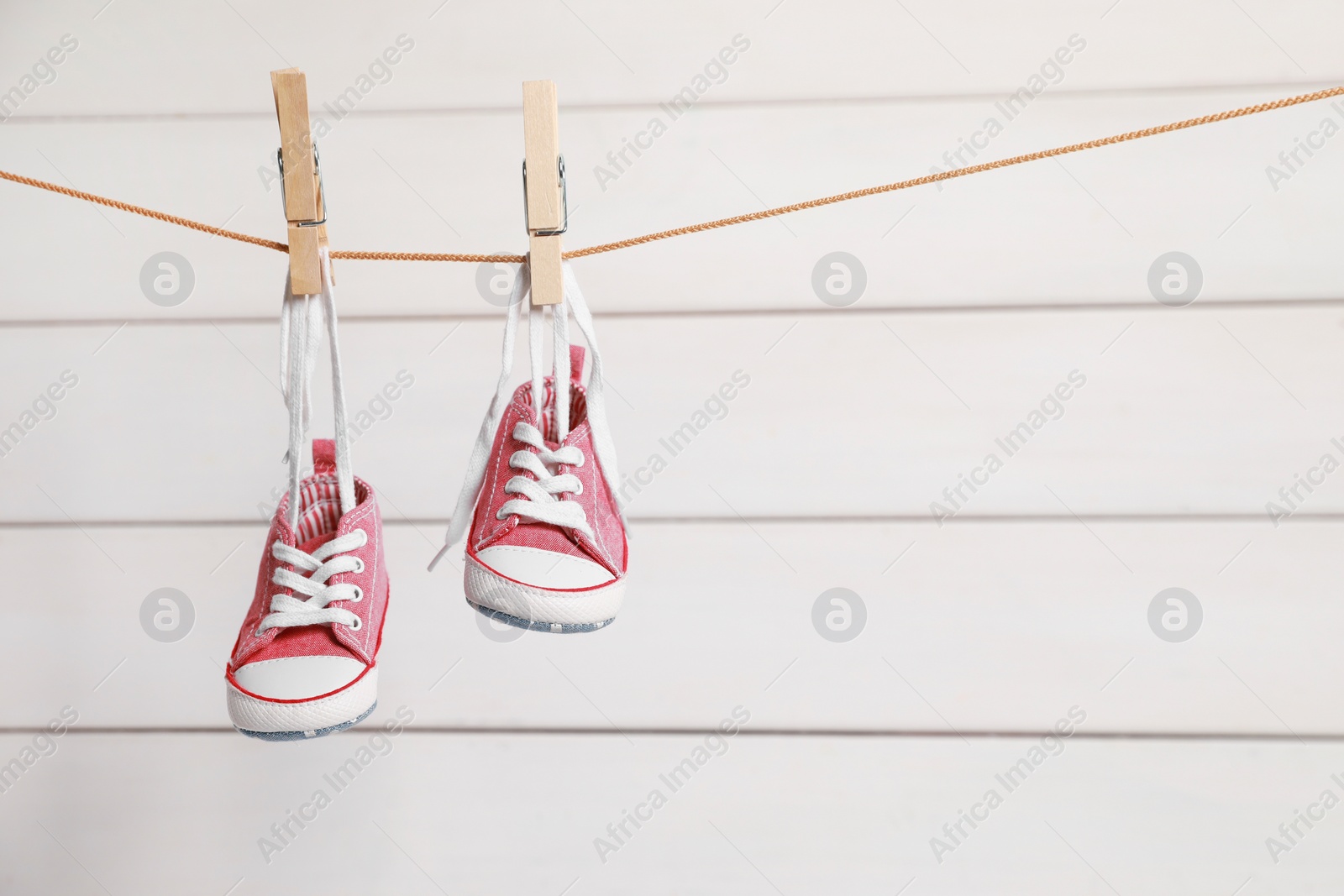 Photo of Cute pink baby sneakers drying on washing line against white wall. Space for text