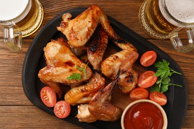 Photo of Mugs with beer, delicious baked chicken wings and sauce on wooden table, flat lay