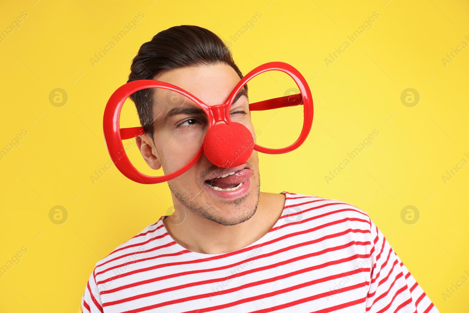 Photo of Funny man with clown nose and large glasses on yellow background. April fool's day