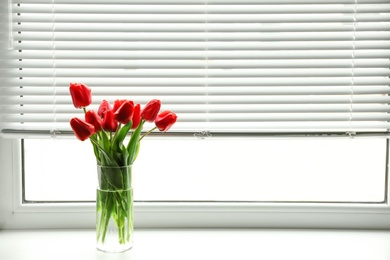 Photo of Bouquet of beautiful tulips in vase near window with blinds. Space for text