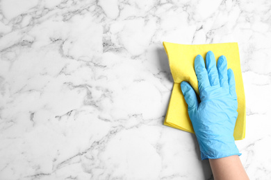 Photo of Woman in gloves wiping white marble table with rag, top view. Space for text