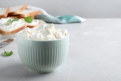 Bowl of tasty cream cheese on grey table. Space for text