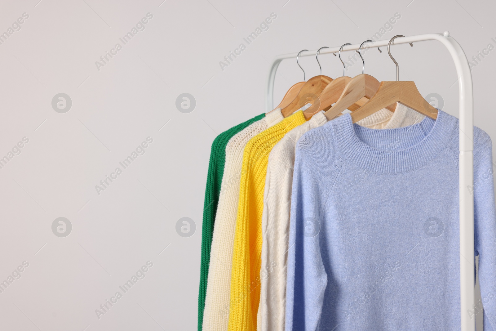 Photo of Rack with different warm sweaters on light background. Space for text