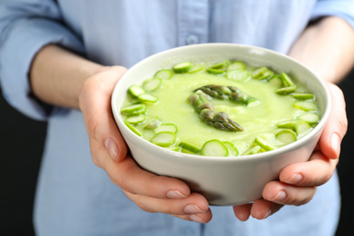 Photo of Woman holding bowl with delicious asparagus soup, closeup