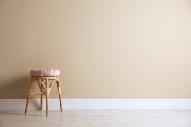 Photo of Stylish wooden stool with cushion near beige wall, space for text. Interior element