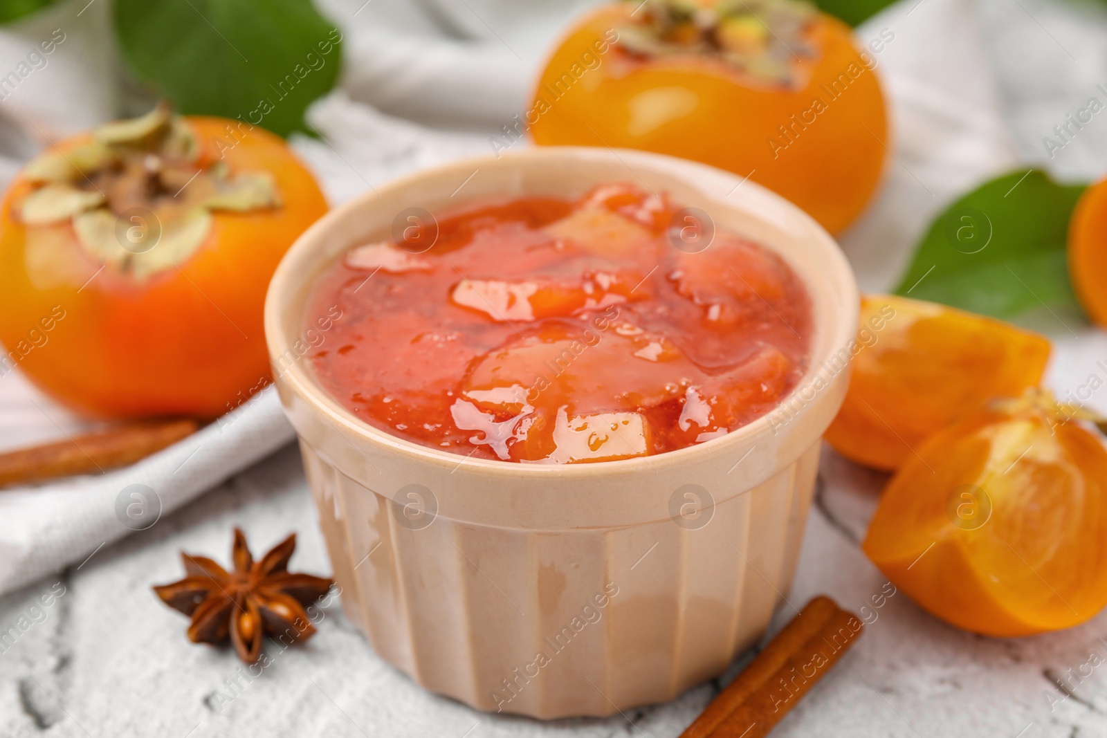 Photo of Bowl of tasty persimmon jam and ingredients on white textured table