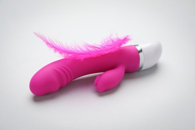 Photo of Pink vaginal vibrator and feather on white background. Sex toy
