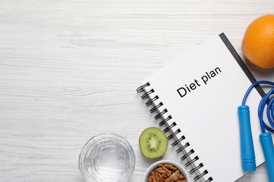 Weight loss concept. Flat lay composition with notebook, skipping rope, glass of water and fruits on white wooden table, space for text