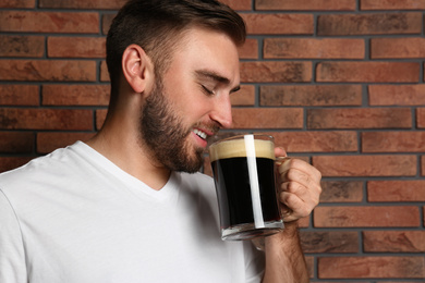 Photo of Handsome man with cold kvass near brick wall. Traditional Russian summer drink