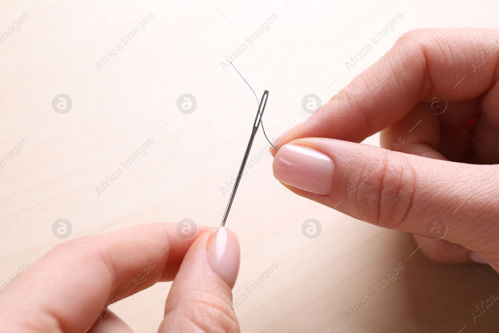 Photo of Woman threading sewing needle at table, closeup