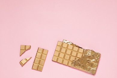 Photo of Shiny golden chocolate bar and pieces with foil on pink background, flat lay. Space for text