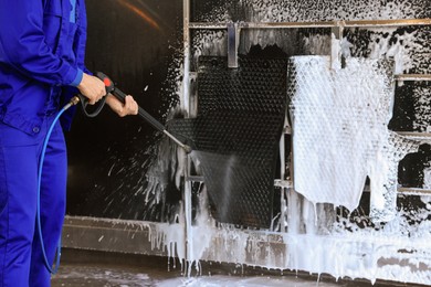 Photo of Worker cleaning auto mats with high pressure water jet at car wash, closeup