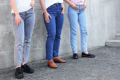 Photo of Women in stylish jeans near grey wall outdoors, closeup