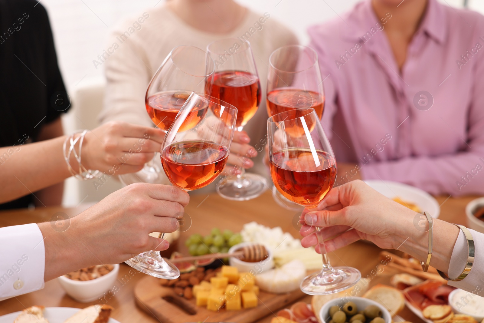 Photo of People clinking glasses with rose wine above table indoors, closeup