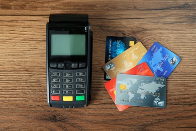 Photo of Modern payment terminal and credit cards on wooden table, flat lay