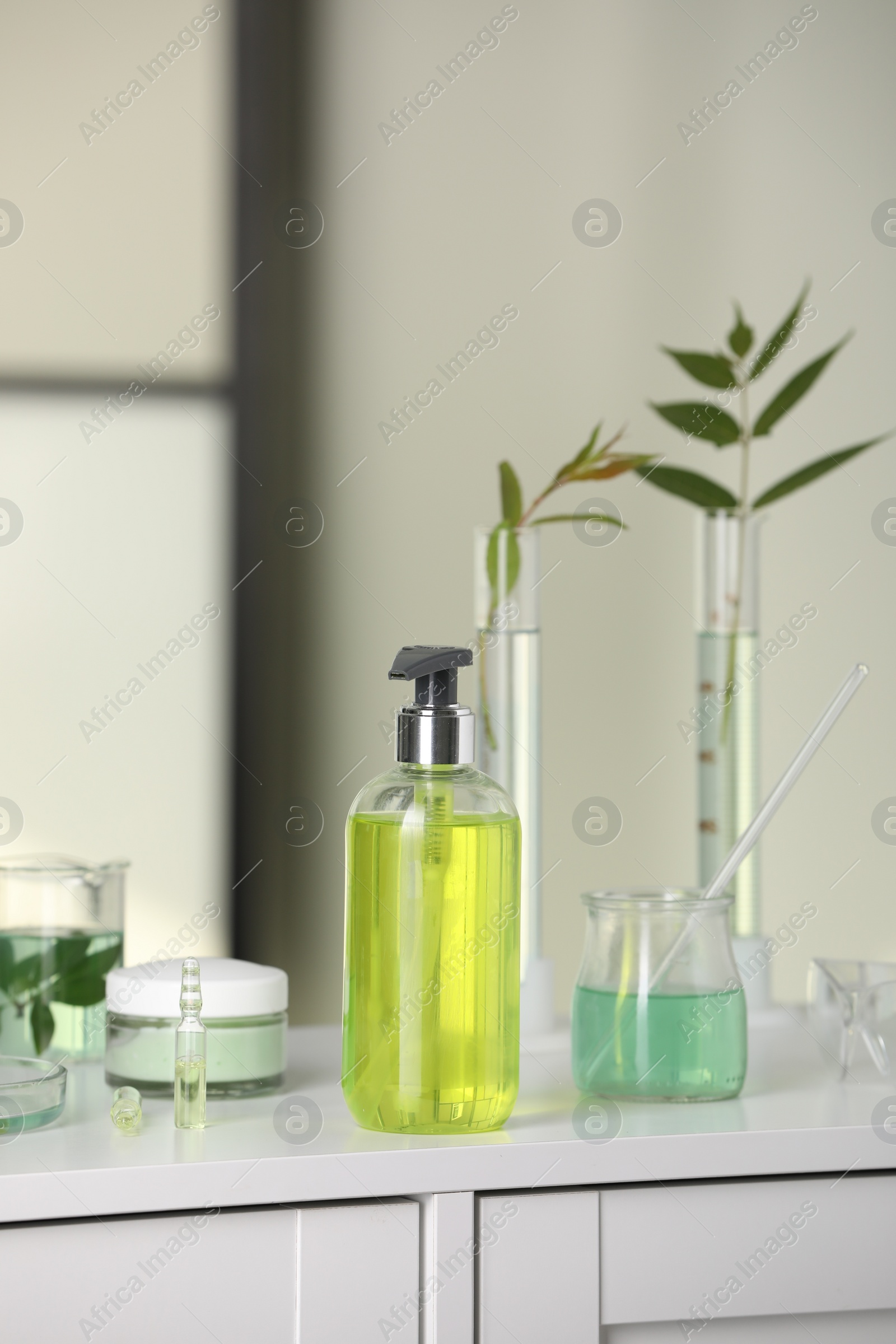 Photo of Bottle and glass tubes with leaves on white lab drawer indoors