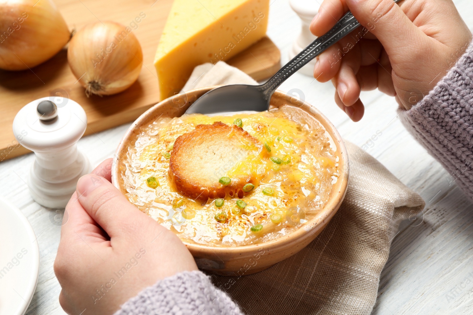 Photo of Woman eating tasty homemade french onion soup at white wooden table, closeup