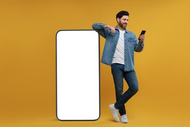 Image of Man with mobile phone standing near huge device with empty screen on orange background. Mockup for design