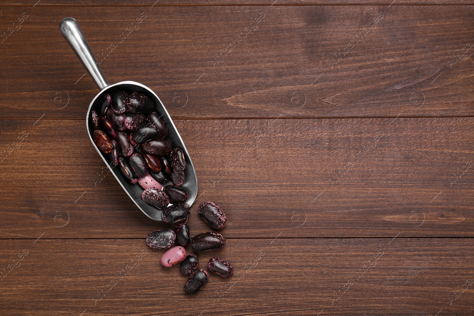 Photo of Metal scoop with dry kidney beans on wooden table, flat lay. Space for text