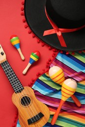 Mexican sombrero hat, maracas, guitar and colorful poncho on red background, flat lay