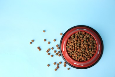 Photo of Dry dog food and feeding bowl on light blue background, flat lay. Space for text