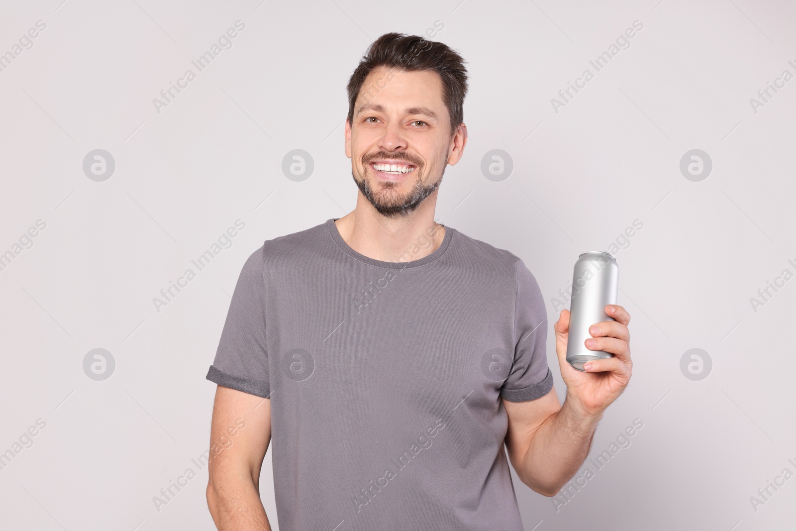 Photo of Happy man holding tin can with beverage on light grey background