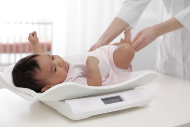 Photo of Doctor weighting African-American baby on scales in light room