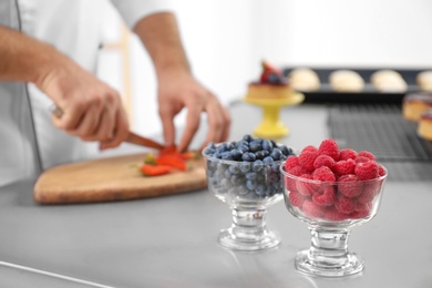 Dessert bowls with berries and blurred view of pastry chef on background