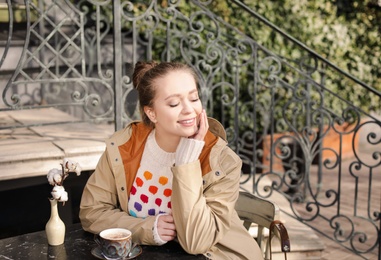 Young woman enjoying tasty coffee at table outdoors