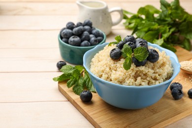 Photo of Tasty quinoa porridge with blueberries and mint in bowl on light table. Space for text