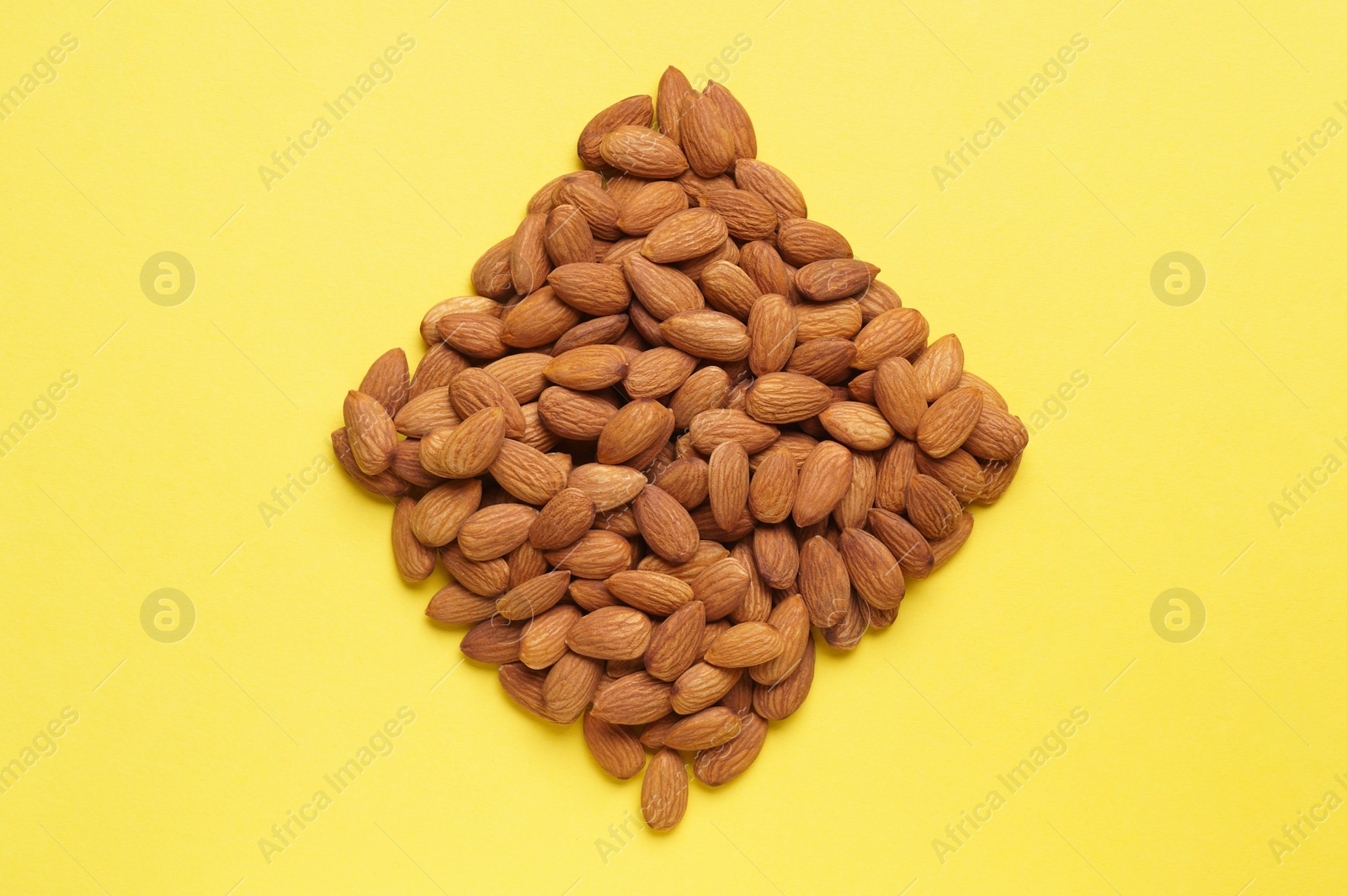 Photo of Rhombus made of delicious raw almonds on yellow background, flat lay