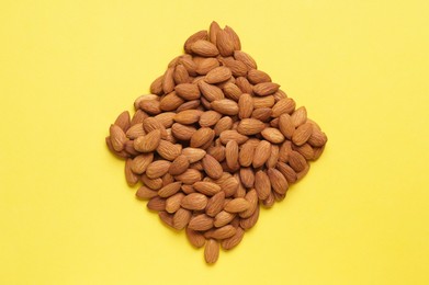 Rhombus made of delicious raw almonds on yellow background, flat lay