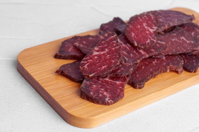 Photo of Pieces of delicious beef jerky on white textured table, closeup