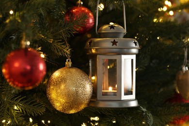 Photo of Christmas lantern with burning candle and balls on fir tree as background, closeup