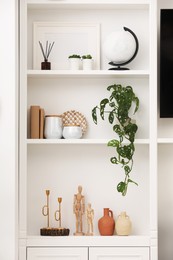Photo of Stylish shelves with decorative elements and houseplant near white wall. Interior design