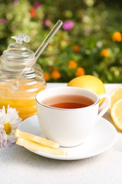 Photo of Cup of delicious tea with honey, lemon and chamomile on white table outdoors