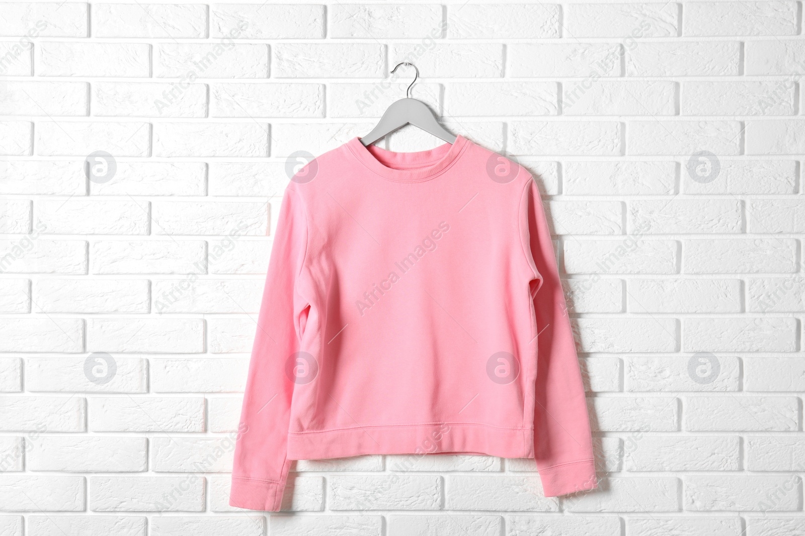 Photo of Hanger with pink sweatshirt against brick wall. Mockup for design