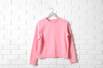 Photo of Hanger with pink sweatshirt against brick wall. Mockup for design