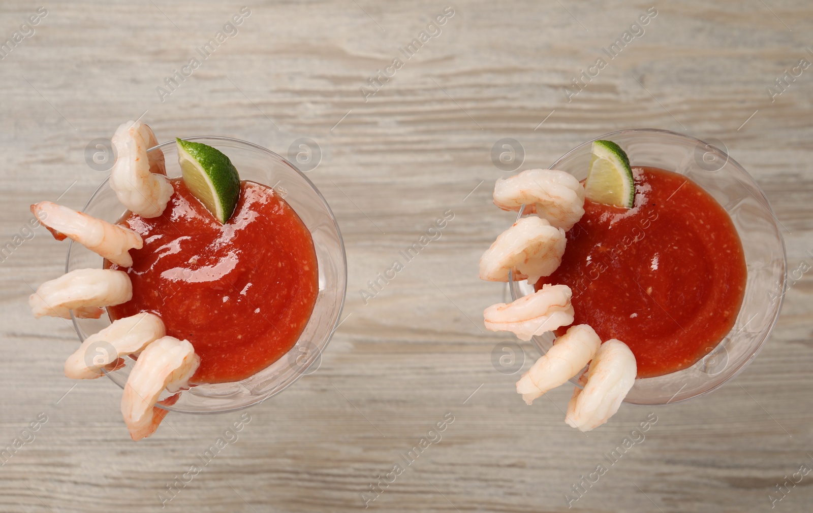 Photo of Tasty shrimp cocktail with sauce and lime in glasses on wooden table, flat lay