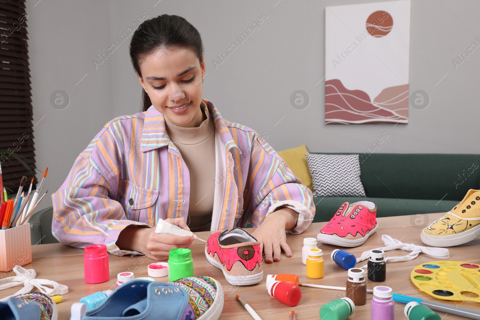 Photo of Woman painting on sneaker at wooden table indoors. Customized shoes